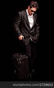 Business man looking down with his luggage on black isolated background