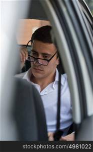 Business man on back seat of car puts on glasses