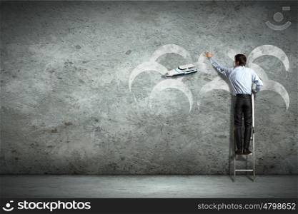 Business man on ladder. Businessman standing on ladder and pointing on picture on wall