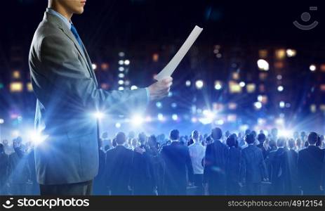 Business man on stage. Back view of businessman speaker standing on podium in lights