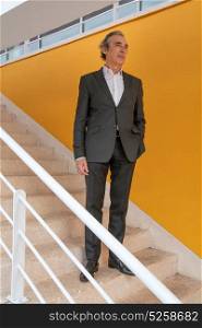Business man on the stairs with a yellow wall behind