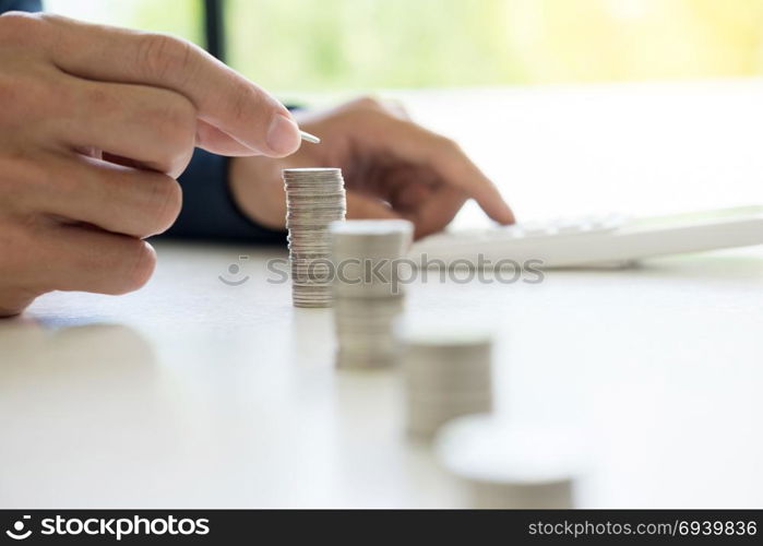 Business man putting coin to rising pile of money and calculator, Saving money investment and financial concept