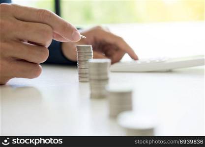Business man putting coin to rising pile of money and calculator, Saving money investment and financial concept