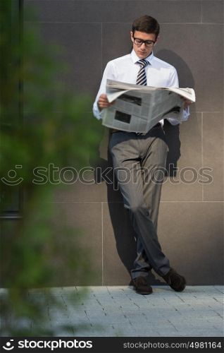 Business man reading a newspaper on the street leaning on wall of modern building
