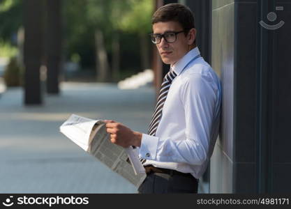 Business man reading a newspaper on the street leaning on wall of modern building