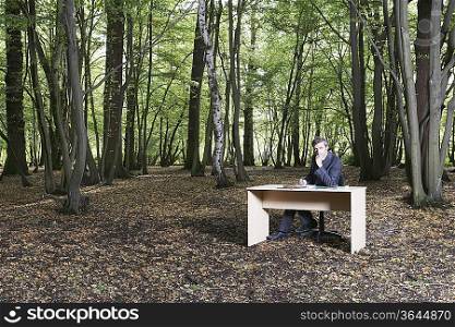 Business man sitting at desk in middle of forest