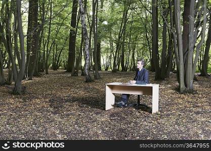 Business man sitting at desk in middle of forest thinking
