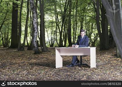 Business man sitting at desk in middle of forest, working