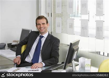 Business man sitting at desk in office, smiling, portrait