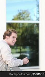 Business man smiles as he leans over glass wall in front of building
