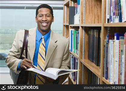 Business man standing by bookshelf, portrait
