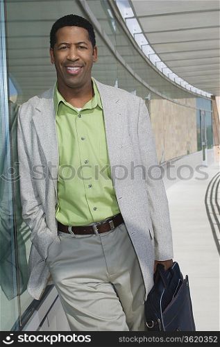 Business man standing by window, outside office building, portrait