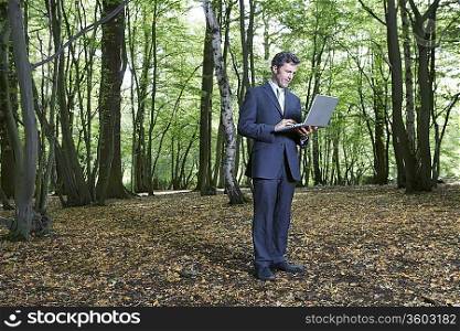 Business man standing in middle of forest typing on laptop