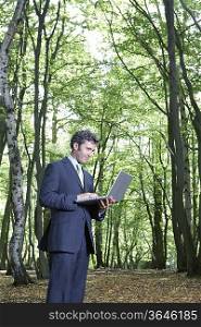 Business man standing in middle of forest typing on laptop
