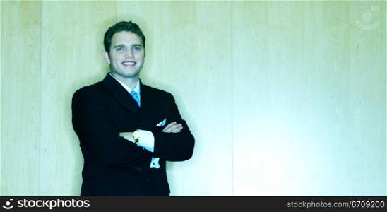 Business Man stands in front of a wood wall with his arms folded and with a smile