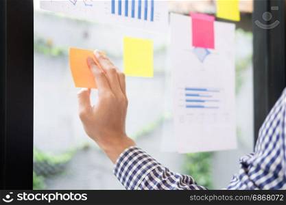 business man sticking adhesive notes on glass wall in office and discussting with team.