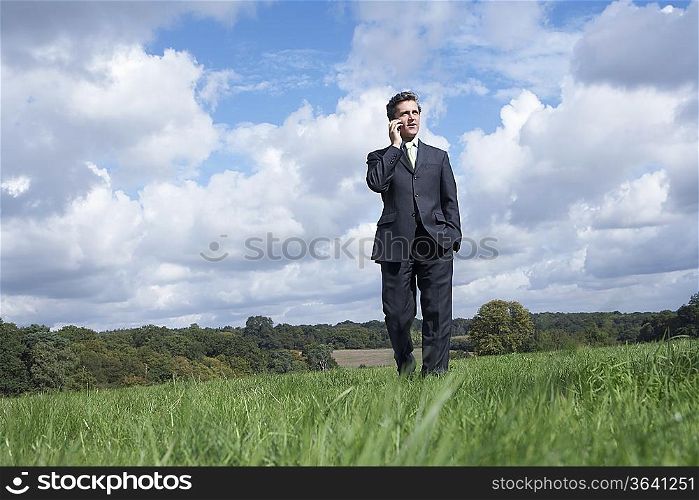Business man talking on mobile phone in field