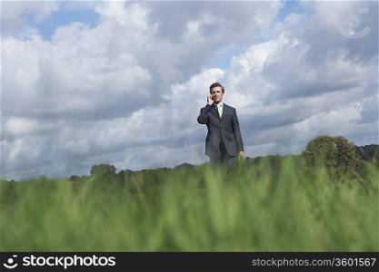 Business man talking on mobile phone in field, selective focus