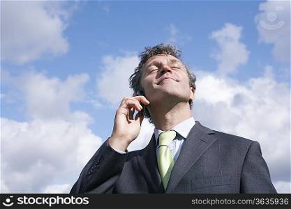 Business man talking on mobile phone, smiling, sky in background