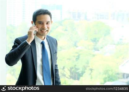 Business man talking smart phone by windows with city view, inside office building background, businessman on phone