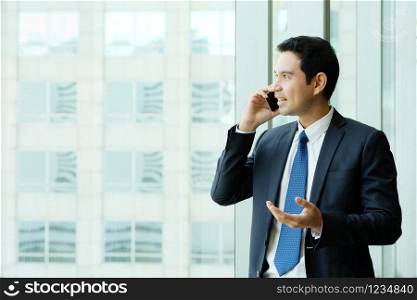Business man talking smart phone by windows with city view, inside office building background, businessman on phone