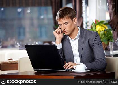 Business man talks to the laptop on mobile in cafe