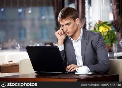 Business man talks to the laptop on mobile in cafe