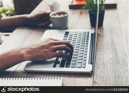 Business man typing laptop and holding coffee cup on wood table.