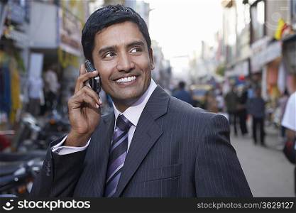 Business man using cell phone on city street, smiling