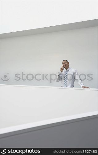 Business man using mobile phone standing by hallway balustrade