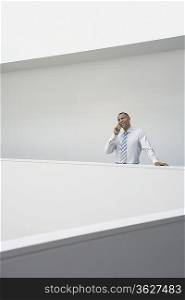 Business man using mobile phone standing by hallway balustrade