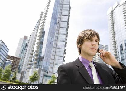 Business man using mobile phone, standing outside office buildings