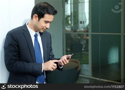 Business man using smart phone with happy smiling face standing in front of meeting room inside office building background, businessman on smart phone, online conferance concept