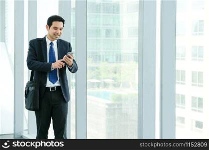Business man using smart phone with happy smiling face while walking by window with the city view, inside office building or airport background, businessman on smart phone
