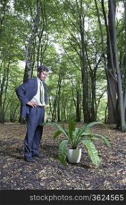 Business man watching potted plant in middle of forest