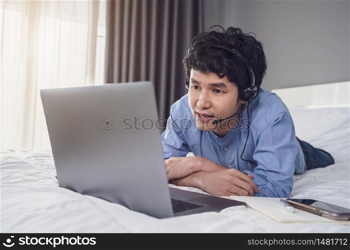 business man wear headset video conference calling on laptop computer on a bed, work from home concept