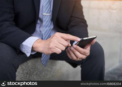 business man wearing black suit and using modern smartphone in outdoor.