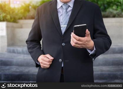 business man wearing black suit and using modern smartphone in outdoor.