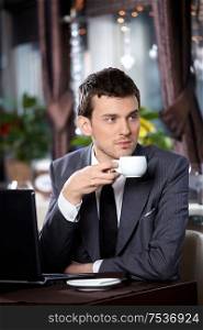 Business man with the laptop drinks coffee in cafe