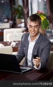 Business man with the laptop smiles and looks at a mobile phone
