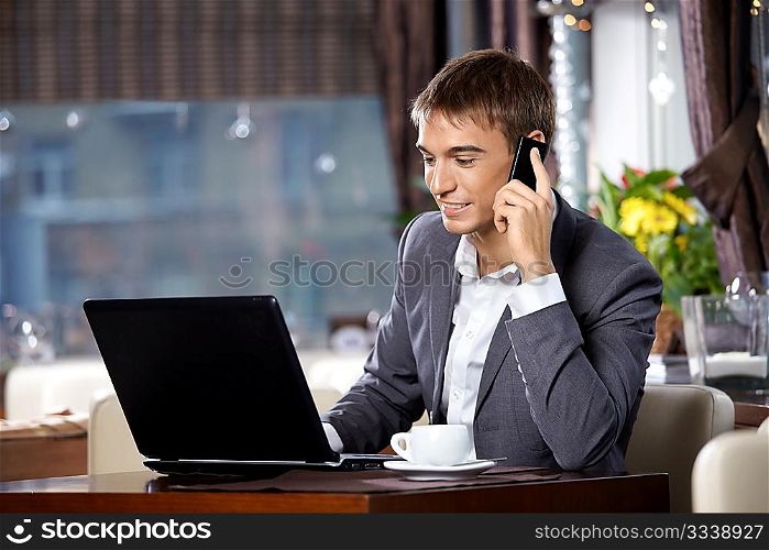 Business man with the laptop uses a mobile communication in cafe