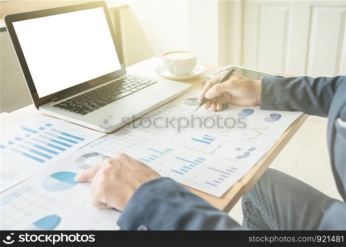 Business man working at office with laptop, and financial graph data documents on his desk.