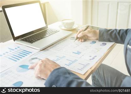Business man working at office with laptop, and financial graph data documents on his desk.