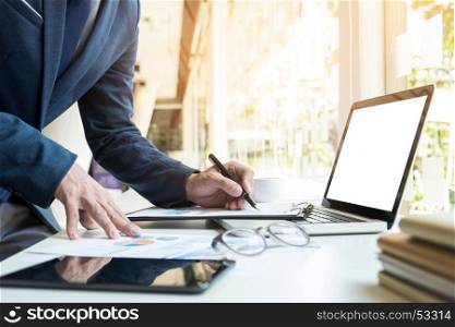 Business man working at office with laptop, tablet and graph data documents on his desk.