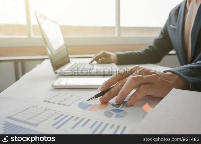 Business man working at office with laptop, tablet and graph data documents on his desk.