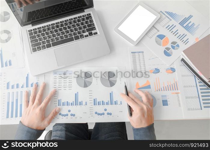 Business man working at office with laptop, tablet and graph data documents on his desk.Top view