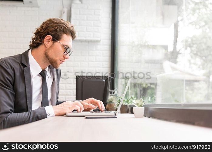 Business man working hard with laptop on desk in office near window. Business and Success concept. People and Occupation concept. Technology and Computer theme. Indoors and interior theme