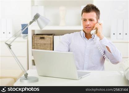 Business man working on laptop computer at home and calling on phone.