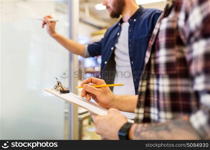 business, manufacture and people concept - men writing to clipboard and whiteboard at office. men writing to clipboard and whiteboard at office. men writing to clipboard and whiteboard at office