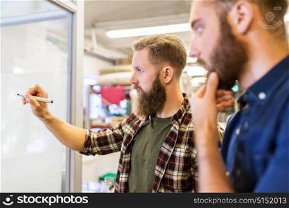 business, manufacture and people concept - men writing to whiteboard at office. men writing to whiteboard at office